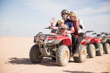 The joyful young family sitting on the ATVs in the desert