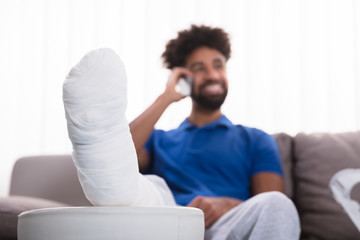 Happy Young Man With Broken Leg Talking On Mobile Phone