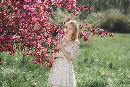 Beautiful young blonde woman enjoying sunny day in park during cherry blossom season on a nice spring day