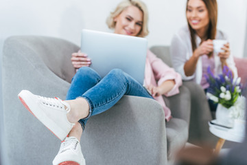 selective focus of girl using laptop while her friend holding cup of coffee