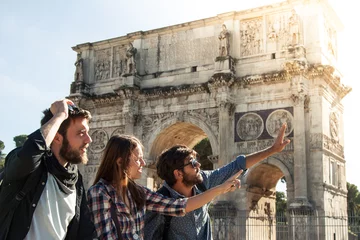 Papier Peint photo Rome Three happy young friends tourists standing in front of Arch of Constantine in rome pointing directions. Lens flare.