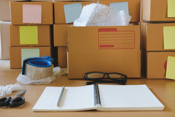 Fototapeta premium notebook, packing accessories at workplace of startup small business owner. cardboard parcel box for online selling. entrepreneur seller desk. e-commerce, shipping concept