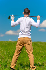 golfer resting with a golf club on his shoulders in a green field, view from the back