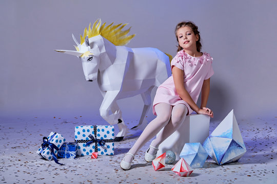 Fashion kid. Designer collection. White big unicorn origami made of paper. Girl in beautiful pink dress. Studio shot.