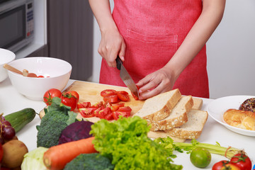 close up of hand cutting tomato on board in kitchen room