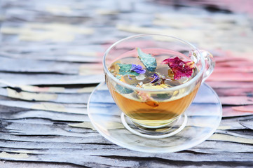 A transparent cup with floral tea on an interestingly cracked old surface.

