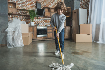 adorable cute little boy with mop cleaning new apartment after relocation