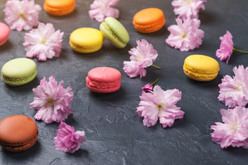 Colorful macaroons with spring sakura flowers on black backround. Selective focus.