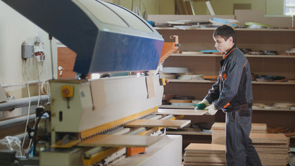 Worker carpenter handles wooden furniture parts on the machine on the factory