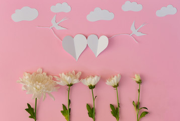 White paper hearts and real flowers on pink background
