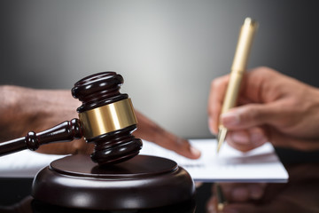 Gavel In Front Of Person's Hand Signing Legal Document