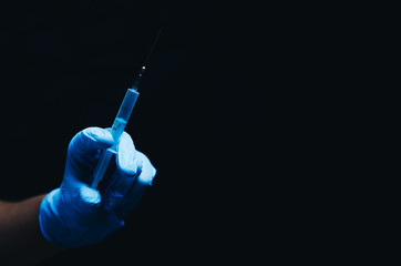 in the hand in a blue glove syringe on black background