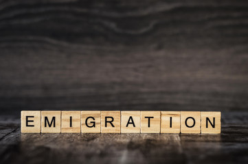 the word emigration is made of bright wood cubes with black letters on a dark wooden background