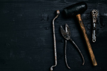 Old, rusty tools lying on a black wooden table. Hammer, chisel, metal scissors, wrench.