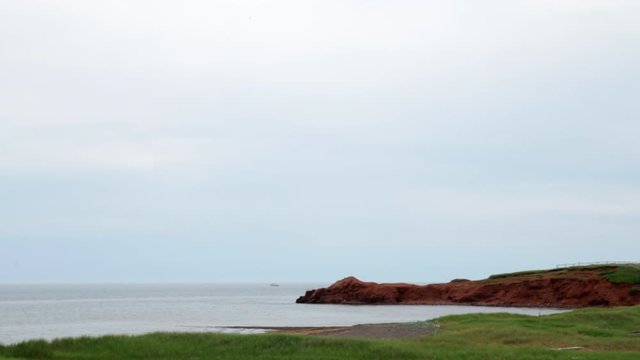 Sand cliff of Magdalen Islands shore with boat on horizon.