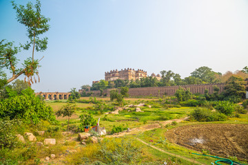 Fototapeta na wymiar Orchha Palace, sunny day and blue sky, green landscape and cultivated fields around. Also spelled Orcha, famous travel destination in India.