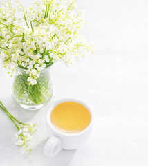 Bouquet of Lilies of the Valley and   cup of tea    on white wooden  table.