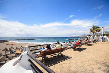 People sit on benches looking to beach in Las Americas, Tenerife, Canary Islands