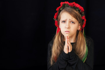 The young girl has folded her hands in prayer on black background. She prays for her country Ukraine