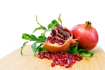 Image of the pomegranate fruits on the wooden plate showing beautiful red color if its seeds, and isolated on white background with embedded clipping path.