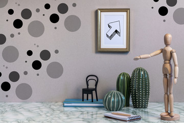 Marble desk with cactuses, wooden doll, notebook, pencil, blue book, gold frame with an arrow and dots on the wall