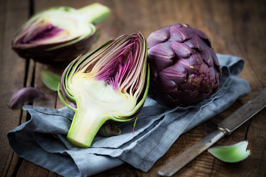 Fresh purple artichokes on dark rustic wooden background with slices of lemon