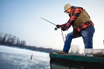 Fotobehang Fisherman draws hooked fish from frozen water © luckybusiness