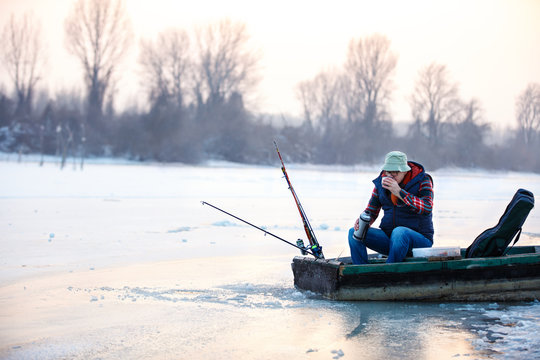 Man in boat drinking tea while fishing fish on winter