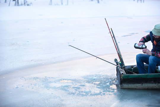 Fisherman fishing in frozen river on winter and drinking tee