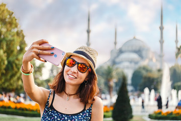 Happy woman in hat and sunglasses making selfie by the smartphone on the background of the Blue...