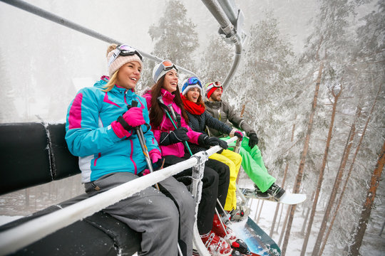 friends enjoying in winter vacations. They ride up ski lift at snowy day