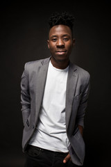 Close-up portrait of handsome black man with charming smile. Studio shot of well-dressed african guy wears white T-shirt and gray jacket.