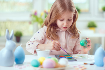 Happy pretty child girl having fun during painting eggs for easter in spring