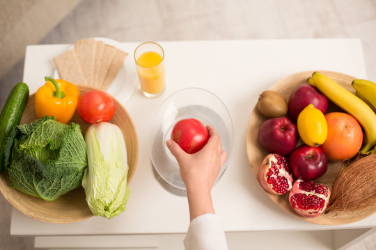 Close up image of fruit and vegetables on plates on table. Woman hand holding tomato.
