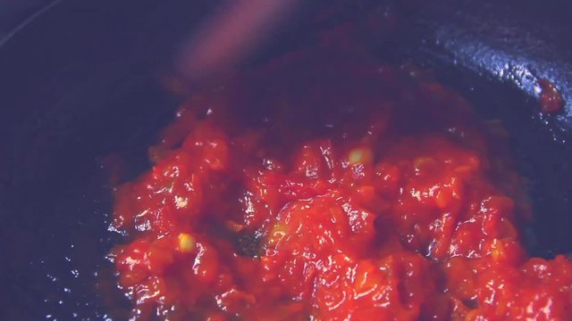 Cooking and mixing delicious and tasty bright red homemade tomato sauce with a big wooden stirring spoon