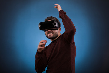 Young happy man experiencing virtual reality through a VR headset isolated on blue,Studio shot