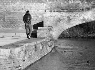 man walking alone by river bridge