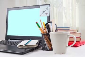 Laptop on the student's desk, on the monitor a sticker with the word university.