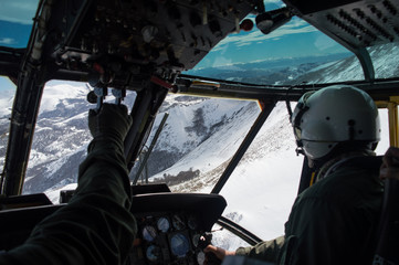 Military helicopter flying through white snowed mountains, pilot and copilot wearing green flightsuit and helmet view © Gonzalo Solari