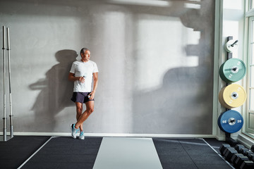 Mature man drinking water after in a gym weight room