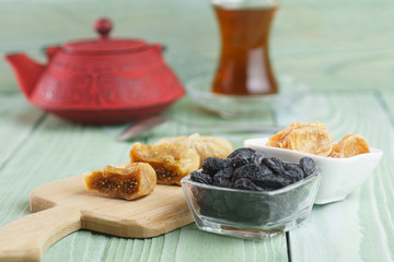 A glass of tea, a red teapot, oriental sweets, raisins, sesame, on a wooden background