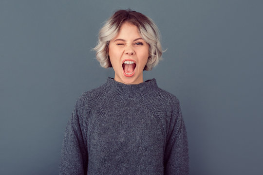Young woman in a grey sweater studio picture isolated on grey background grimase wink