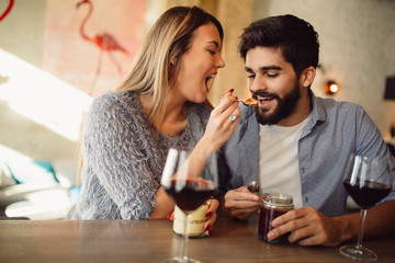Beautiful girl feeding her boyfriend with cake in cafe, drinking wine and celebrating Valentine's day.