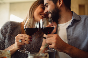 Couple clink glasses with red wine at date in casual outfit in cafe. Couple having romantic moments.