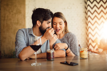 Handsome man feeding his girlfriend with cake. Couple drinking wine and celebrating Valentine's day.