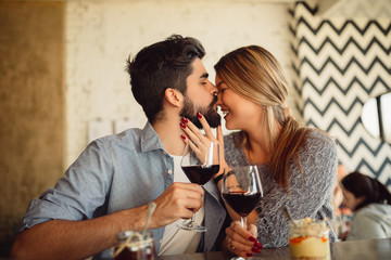 Handsome man kissing his girlfriend in nose. Couple drinking wine a cafe and celebrating Valentine's day.