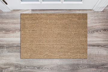 Obraz premium Pusta brązowa wycieraczka z włókna kokosowego przed białymi drzwiami w holu. Mata na drewnianej podłodze, makieta produktu