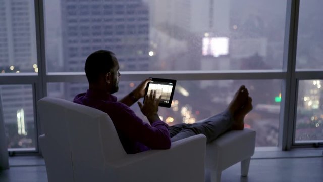 Young man browsing photos on tablet computer at home 4K
