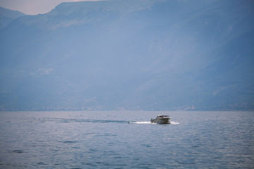 Naklejka premium a fast motor boat sails on the lake lago di garda in Italy against the backdrop of mountains and clouds. Summer in sunny weather