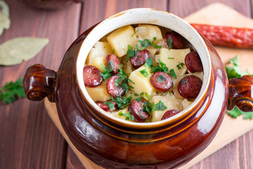 Hot potato goulash with bacon and Vienna sausages served in a ceramic bowl with on an old wooden table